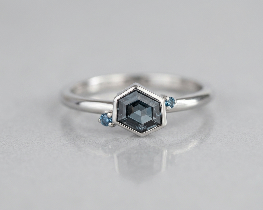 Geometric 9ct white gold stacking ring with an asymmetrical hexagon-cut grey-blue spinel and two blue diamond accents, part of the Geo range. Shot against a soft grey background.