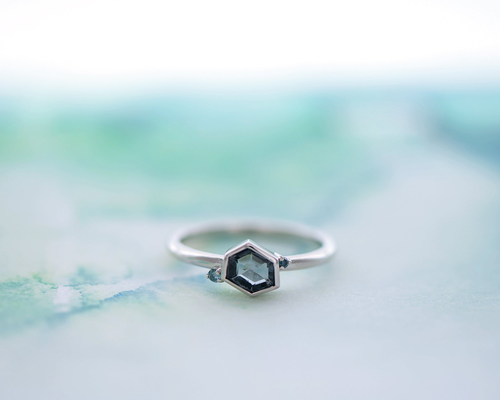 Silver ring with a hexagonal Spinel and two blue diamonds on a blurred background