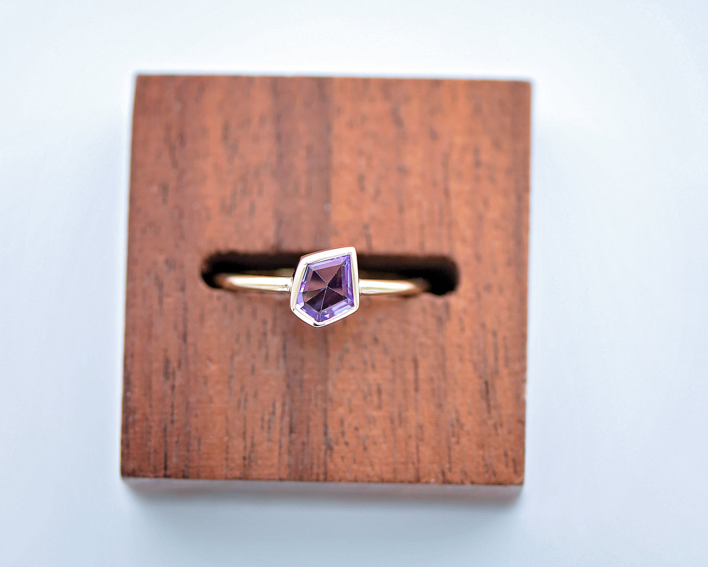 Gold ring with a purple gemstone on a wooden stand against a light blue background