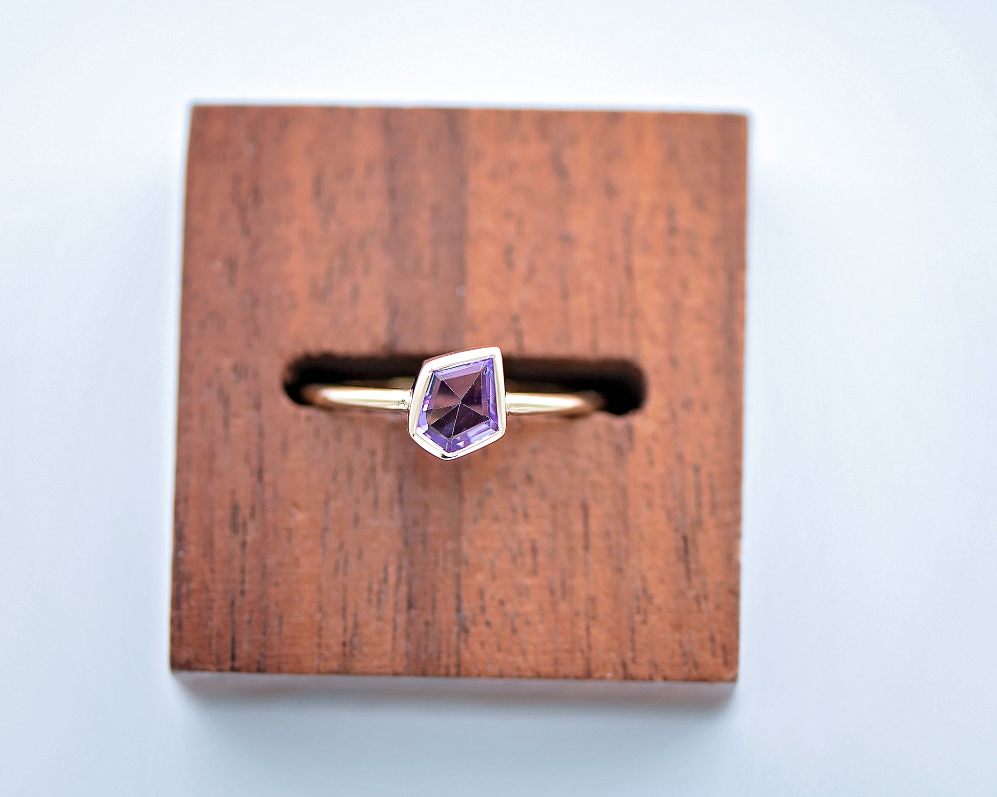 Gold ring with a purple gemstone on a wooden stand against a light blue background