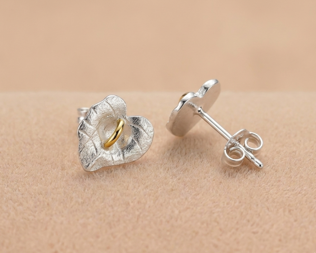 Silver leaf-shaped stud earrings with gold center on beige surface