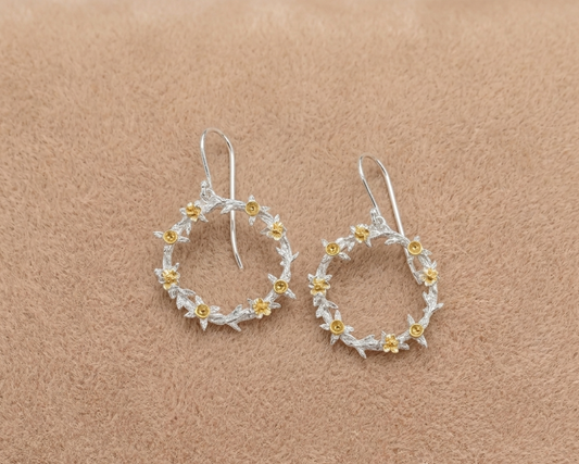 Pair of silver hoop earrings with gold accents on a beige background