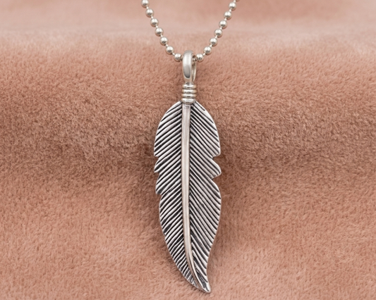 A detailed sterling silver feather pendant with an antique finish to highlight the texture shown on a neutral velvet background.
