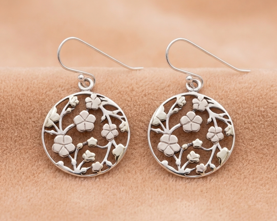 Sterling silver round disc hook earrings featuring an intricate cutout cherry blossom vine design displayed on soft skin-tone velvet.