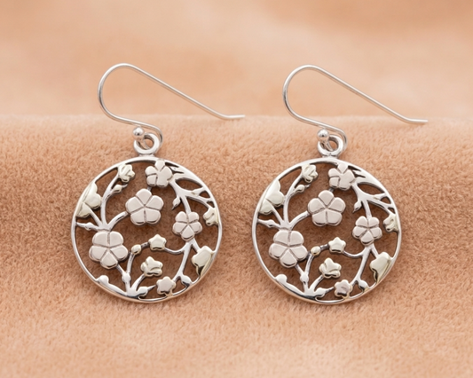 Sterling silver round disc hook earrings featuring an intricate cutout cherry blossom vine design displayed on soft skin-tone velvet.