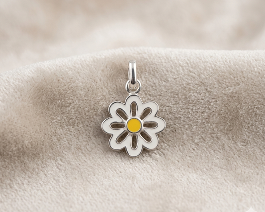 A sterling silver daisy pendant with white enamel petals and a yellow enamel center displayed on soft skin-tone velvet fabric.