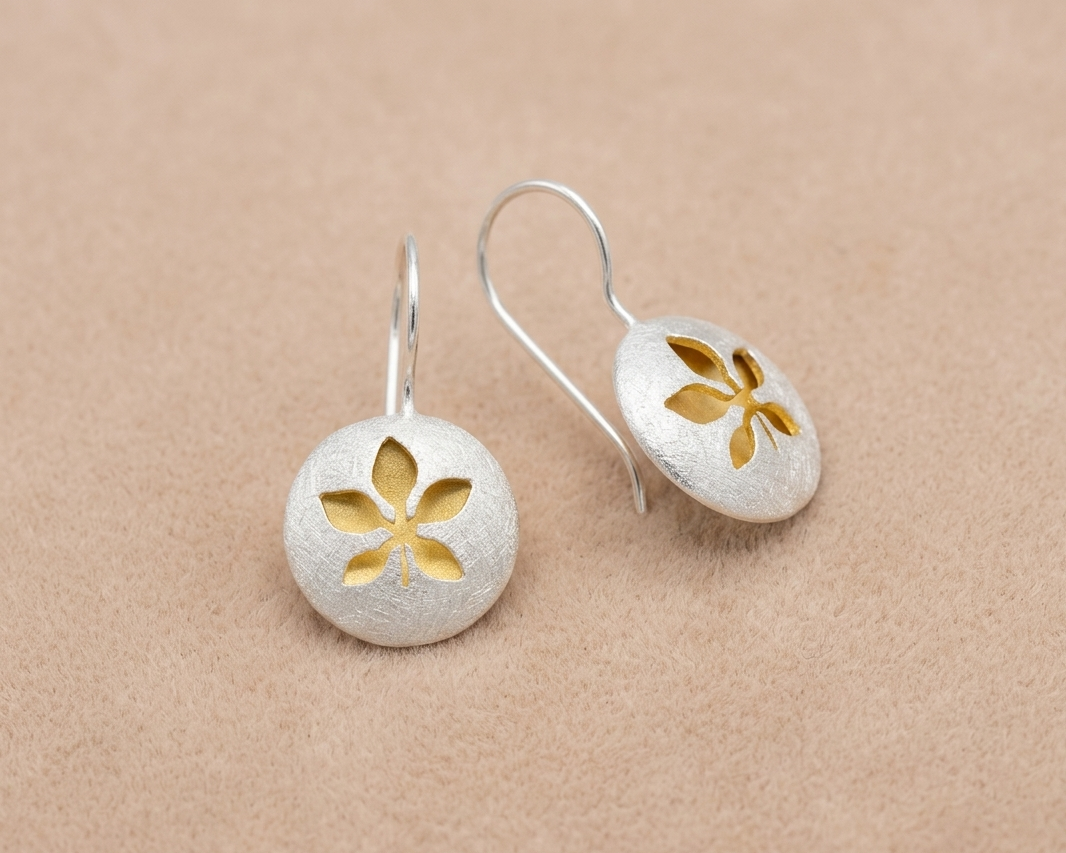 Handcrafted sterling silver heart stud earrings with a textured organic finish and a central yellow gold plated accent resting on soft skin-tone velvet.