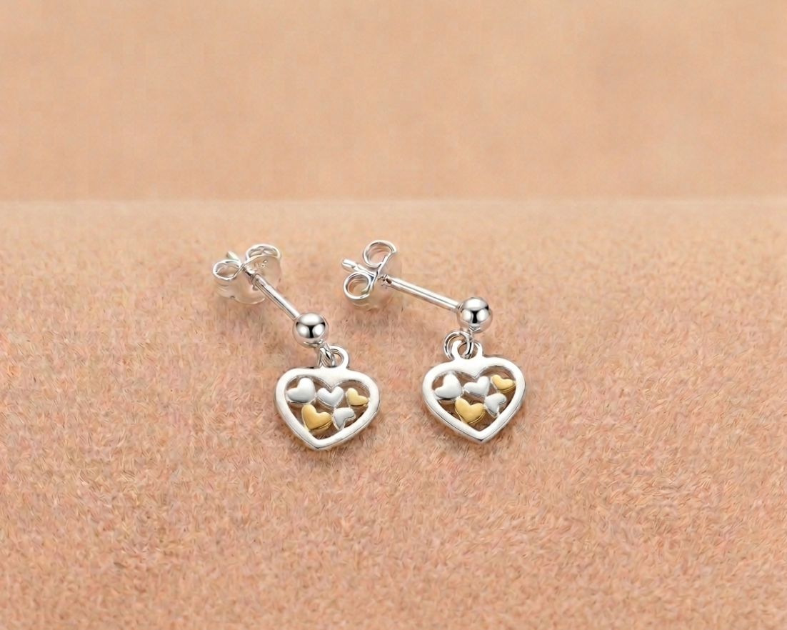 Sterling silver heart drop earrings featuring delicate yellow gold plated heart accents inside the cutout shown on soft skin-tone velvet.