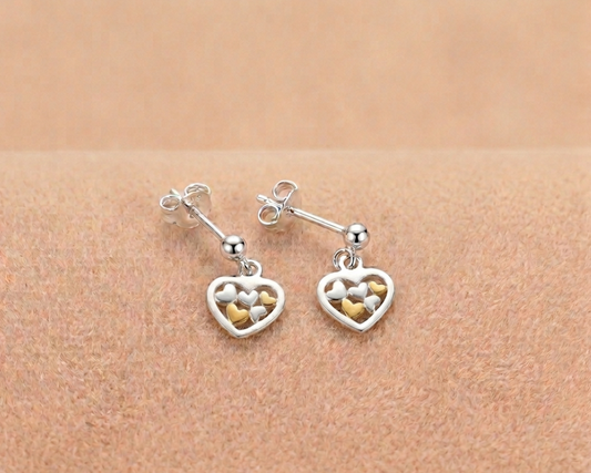 Sterling silver heart drop earrings featuring delicate yellow gold plated heart accents inside the cutout shown on soft skin-tone velvet.